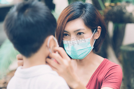 母亲在户外照顾带口罩的儿子以保护流感或 covid-19，妈妈戴上带儿童安全的医用口罩以保护公共场合大流行病的爆发，医学概念。