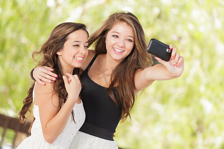 两个迷人的混血女友在户外使用智能手机自拍