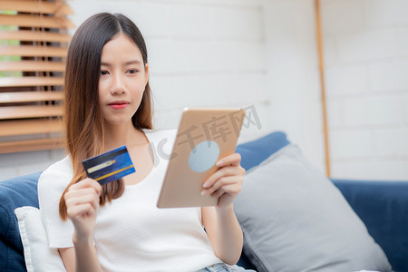 年轻的亚洲女性微笑着拿着信用卡在线购物，使用平板电脑购买和支付，女孩使用借记卡购买或金融交易、生活方式和电子商务概念。