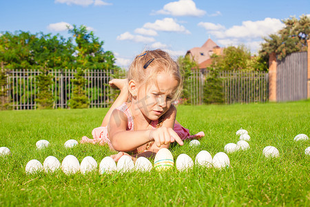 在绿草上玩白色复活节彩蛋的可爱小女孩的画像
