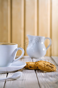 杯子里的咖啡摄影照片_杯子里的咖啡和饼干，白色旧桌上的牛奶碗