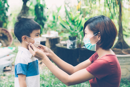 母亲在户外照顾带口罩的儿子以保护流感或 covid-19，妈妈戴上带儿童安全的医用口罩以保护公共场合大流行病的爆发，医学概念。
