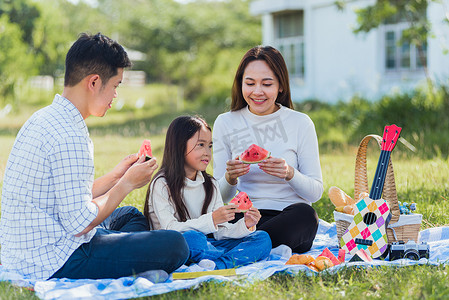在阳光明媚的公园里享受户外坐在野餐毯上吃西瓜的幸福家庭