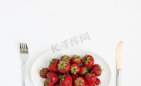 白盘上新鲜多汁的草莓，配上餐具，是