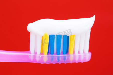 牙刷背景摄影照片_在红色背景中的粉红色牙刷上挤牙膏。