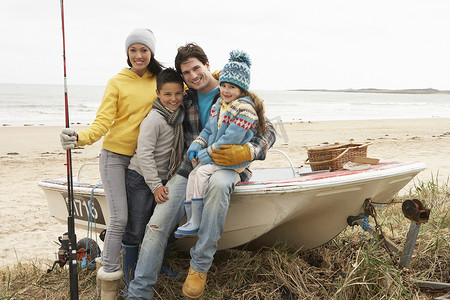 家庭组坐在船上用钓鱼竿在冬季海滩上
