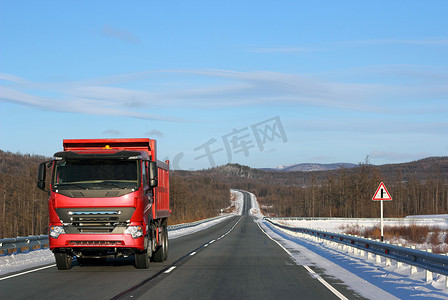 车辆拖车摄影照片_冬季道路上的红色卡车。