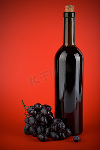 红色背景下的一瓶葡萄酒和葡萄
