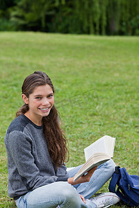 年轻的微笑女孩盘腿坐着，手里拿着一本书