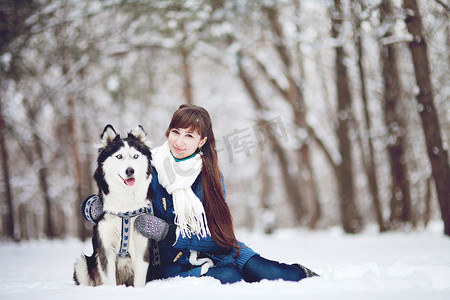 在冬天的森林里，女孩和一只西伯利亚哈士奇狗坐在雪地里