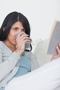 喝水看书摄影照片_女人一边看书一边用杯子喝水