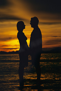日落时分手牵手站在沙滩上的情侣（剪影）