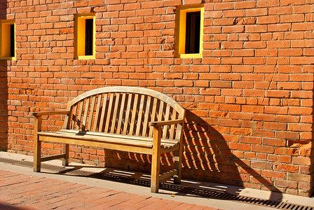 坐在带黄色窗户的橙色砖墙旁的木凳