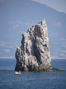 在远处一个大型度假小镇的背景下，蓝色大海中间的一块陡峭的小岩石