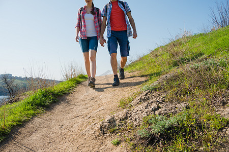 年轻夫妇背着背包在阳光明媚的夜晚在美丽的岩石小径上徒步旅行。