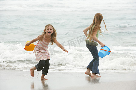 快乐的小姐妹们拿着水桶在沙滩上玩水