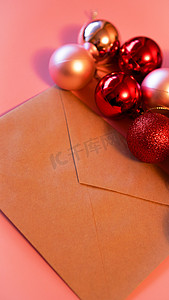 粉红色背景上带有圣诞红和粉红色球的牛皮纸信封
