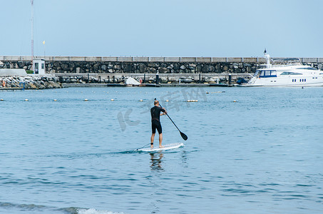 在秘鲁海滩上站起来划桨的人在蓝色的水面上快乐地站在桨板上。