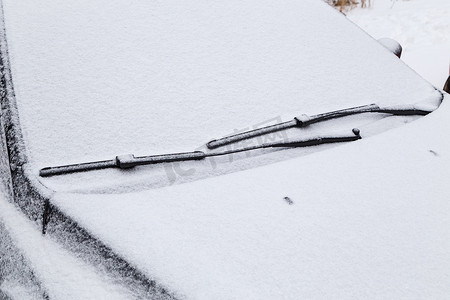 汽车挡风玻璃和刮水器水刀在冬季阴天光下结冰并覆盖着雪