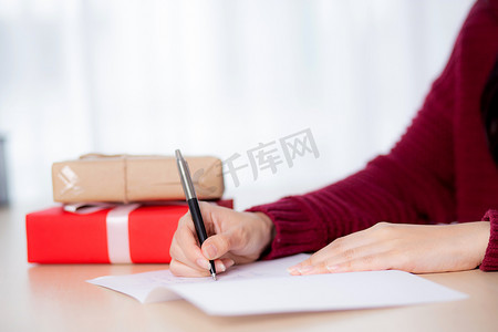 亚洲年轻女性在圣诞节在家、前夕和庆祝时写明信片的特写手，女性在贺卡上写信息，在节日、祝贺和庆祝时赠送礼品盒。