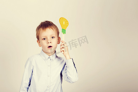 头脑运动摄影照片_有黄色纸电灯泡的逗人喜爱的男孩反对白色背景。