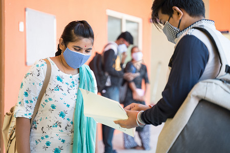 重新开张摄影照片_戴医用口罩的大学生在大学走廊讨论 — covid-19冠状病毒大流行后大学重新开放的概念。