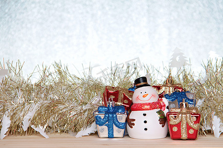 圣诞礼盒红色摄影照片_可爱的雪人、圣诞礼盒或礼物，以及木头、银色闪光背景上的金色飘带或金属丝