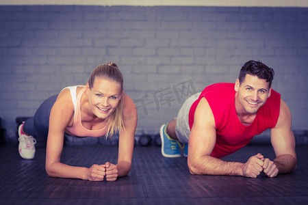 让微笑的情侣在健身房一起做平板支撑