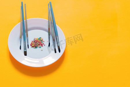 涂色画摄影照片_黄色背景的盘子上涂有不同颜色的刷子和米饭