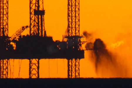 石油燃烧摄影照片_在日落时的石油平台与燃烧的火炬。石油平台的牵引。