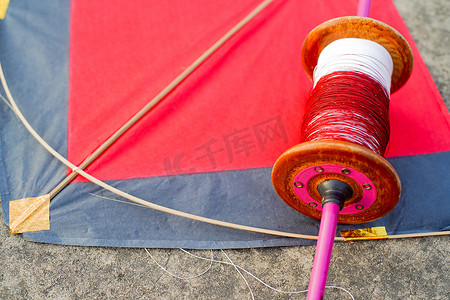 风筝节摄影照片_用红色和黑色纸和木风筝自上而下的平面射击，用木制手工 charkhi 线轴和普通和玻璃覆盖的线，用于在印度 makar sankranti uttarayana 节举行的风筝比赛
