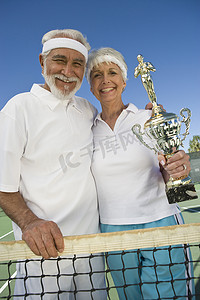 在网球网上拿着奖杯的快乐老年夫妇的肖像