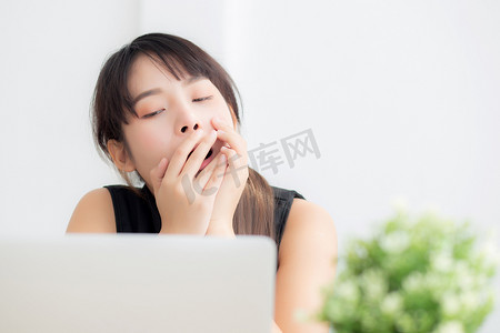 美丽的年轻自由亚洲女性在办公室的笔记本电脑上工作无聊和疲倦，女孩懒惰困倦，在笔记本上打哈欠，女秘书疲惫不堪，商业理念。