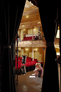 一位年轻女子坐在舞台上拿着剧本的全长侧视图