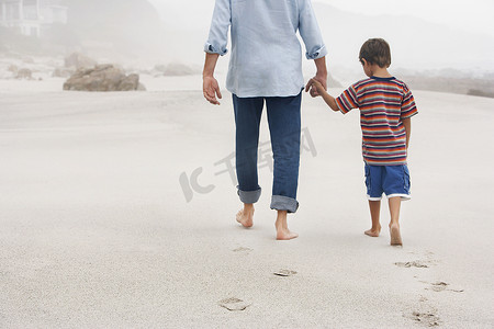 父子手牵手在沙滩上行走的后视图