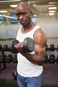 男背心摄影照片_在健身房用哑铃锻炼的肌肉男