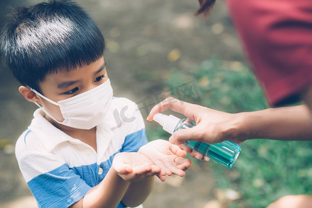 母亲在户外用面罩和消毒剂照顾儿子，以保护流感或 covid-19，母亲和孩子戴着医用面具清洁手，以确保公共流行病爆发的安全。