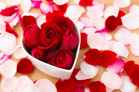 粉色心形花瓣摄影照片_心形碗内美丽的红玫瑰，旁边有花瓣