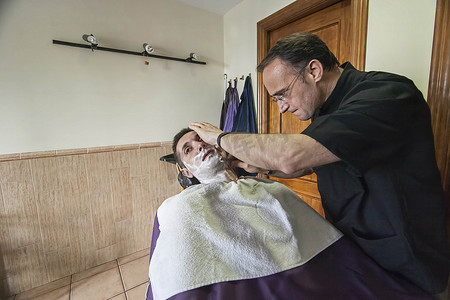 在西班牙安达卢西亚哈恩省萨比奥特的一家理发店里，理发师用剃刀给年轻人剃须