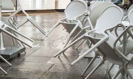 晚上，在意大利下雨后，街边咖啡馆里的湿白色塑料椅子上有雨滴，翻倒了