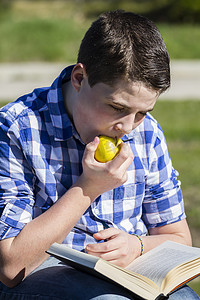 吃。年轻人在户外用黄色苹果看书。