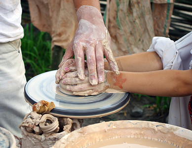 陶工的手帮助孩子在陶器上做一个水罐