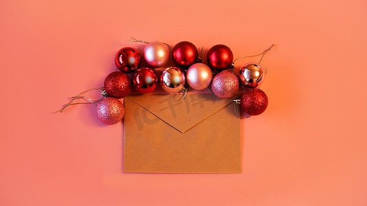 牛皮纸信封摄影照片_粉红色背景上带有圣诞红和粉红色球的牛皮纸信封