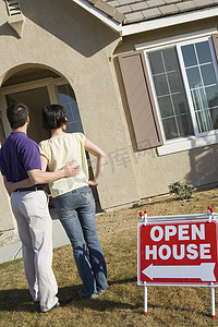 一对成熟夫妇站在带开放式房屋招牌的房子外的后视图