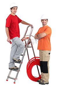两名水管工拿着梯子和铜管站着