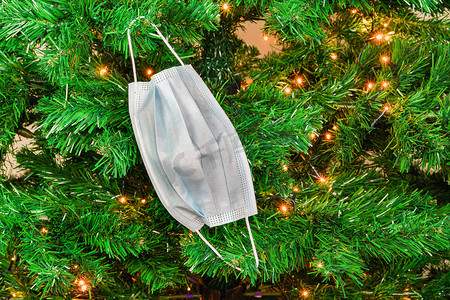 圣诞 covid-19 面具挂在一棵带灯的绿树上作为装饰。