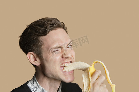 鼠年新年灯笼边框摄影照片_彩色背景下咬香蕉时眨眼的中年男子画像