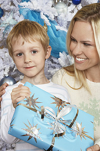 一个可爱的男孩和母亲在圣诞树前拿着礼盒的画像