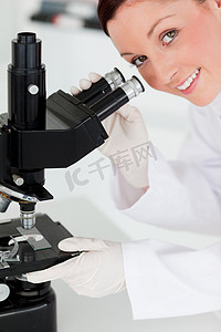 看通过显微镜的迷人的红发科学家