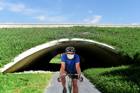 骑自行车的人戴着 COVID-19 外科口罩在自行车道上。